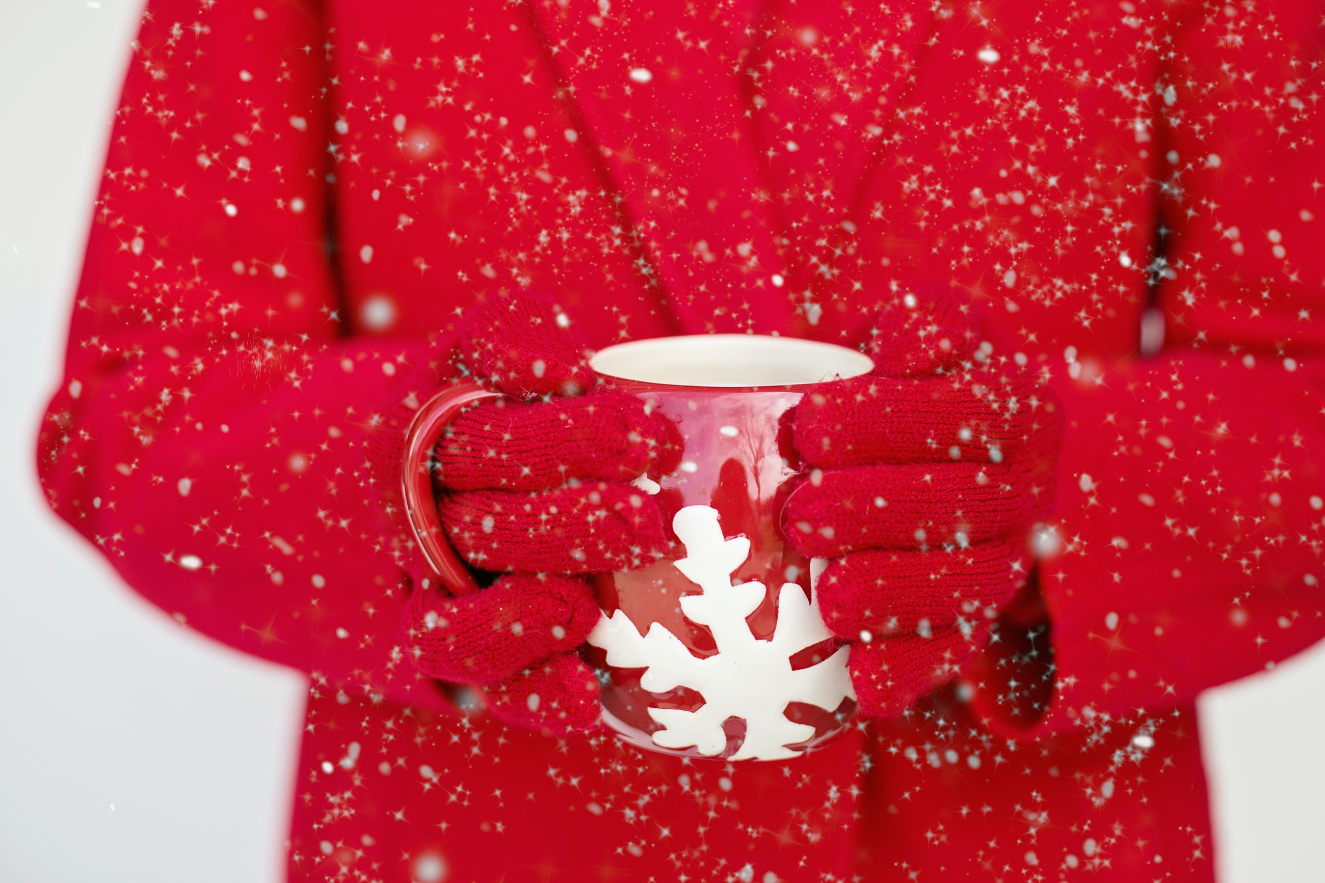 Red gloves hands hold a red mug with a painted white snowflake in front of a red winter coat