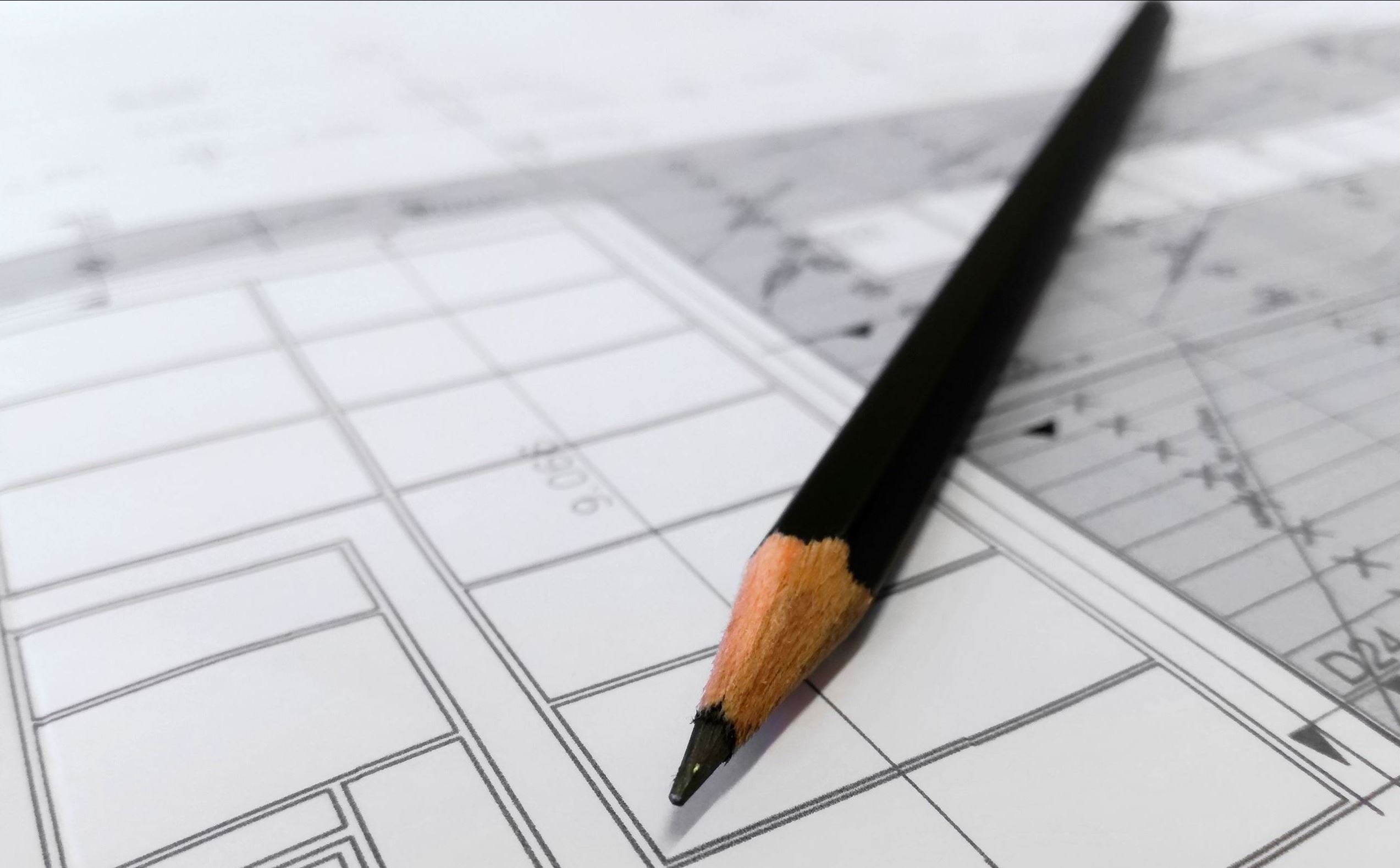 A pencil lays over white paper depicting blueprints 
