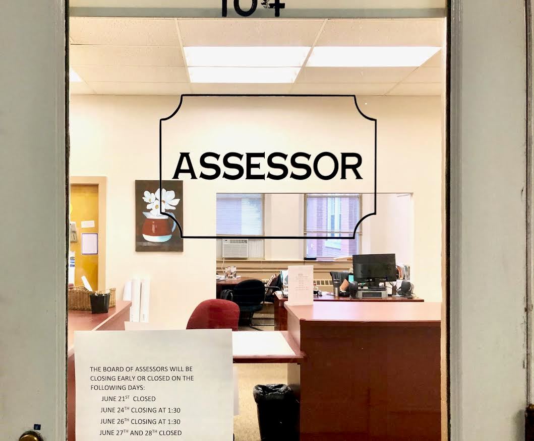 A white wooden door with a window leading into an office titled Assessor's Office 