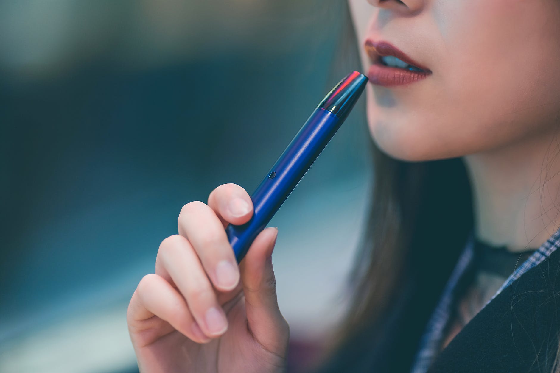 A young woman holds a vape pen to her mouth 