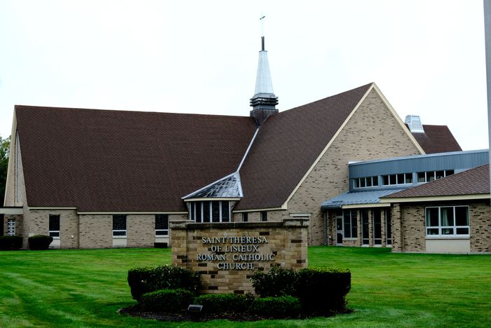 A beige brick church building with a steeple on top set back in green grass