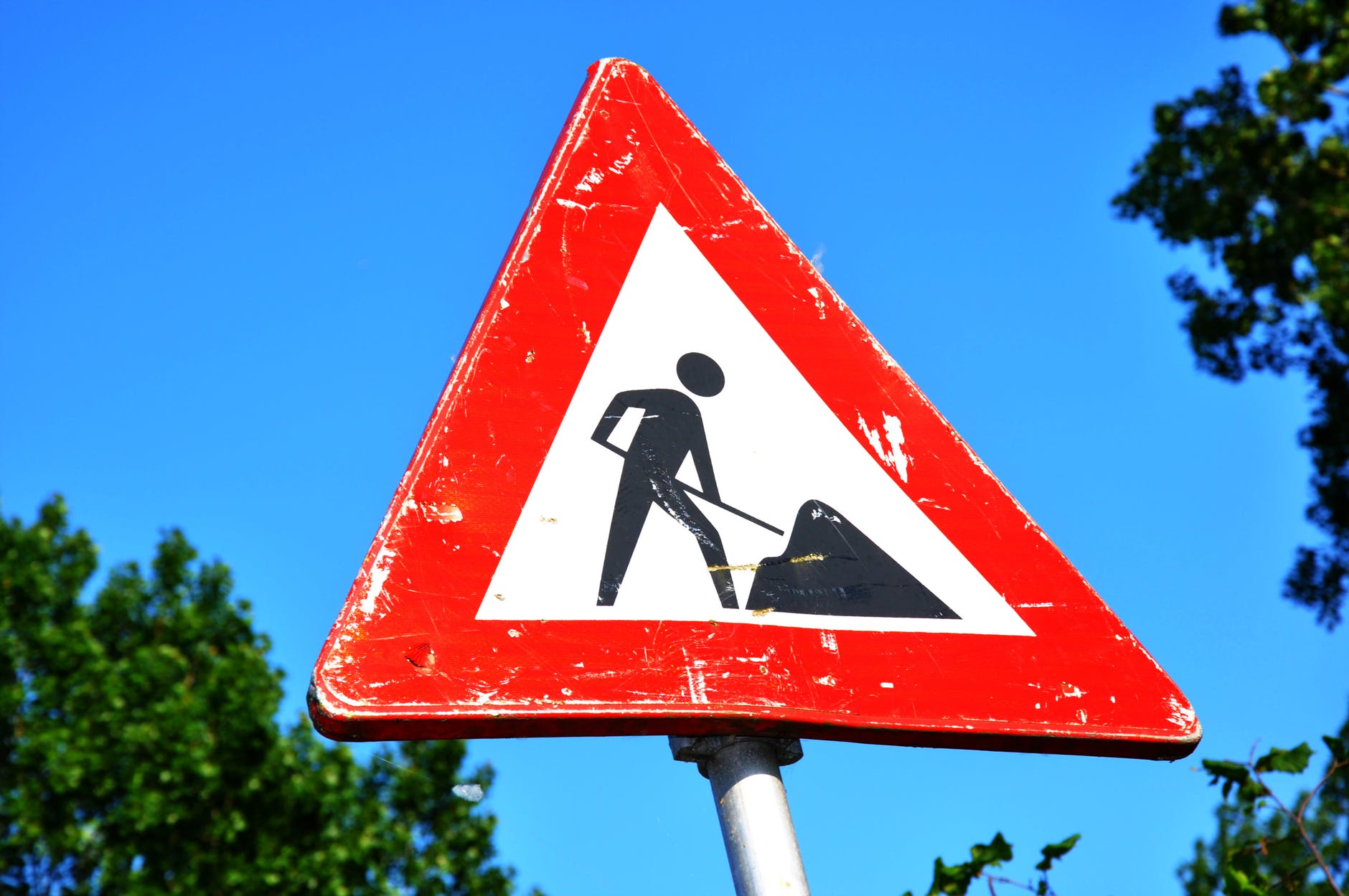 A white triangle-shaped road work sign depicting a human shoveling dirt is outlined in red