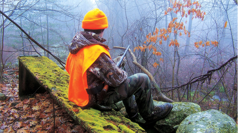 A hunter wearing blaze orange sits on a log